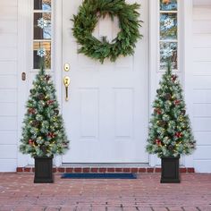 two christmas trees in front of a white door with a wreath on the top and bottom