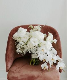 a bouquet of white flowers sitting on top of a velvet chair in front of a wall