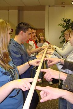 a group of people standing next to each other holding onto a wooden stick with one hand