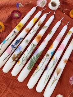 six white candles with flowers painted on them are lined up in a row next to dried daisies and wildflowers