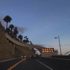 the sign for santa monica is lit up at dusk on an overpass with palm trees in the background