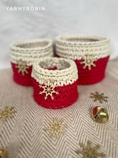 two red and white crocheted baskets sitting on top of a table next to bells