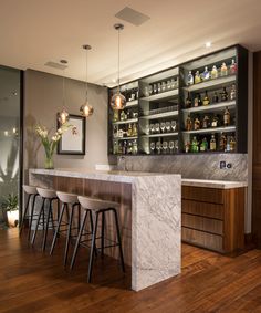 a bar with marble counter tops and stools in front of shelves filled with liquor bottles