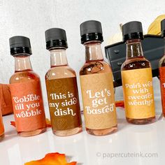 five bottles of different types of alcohol sitting on a white table with autumn leaves around them