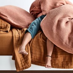 a person laying on top of a bed covered in blankets and pillows with their feet propped up