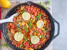 a skillet filled with vegetables and lemons on top of a cutting board