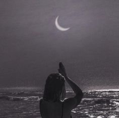 a woman standing on top of a beach next to the ocean under a crescent moon