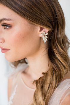 a woman with long hair wearing a white dress and earrings on her head, looking off to the side