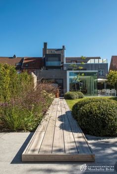 a wooden walkway in front of a building with lots of plants and bushes on the side