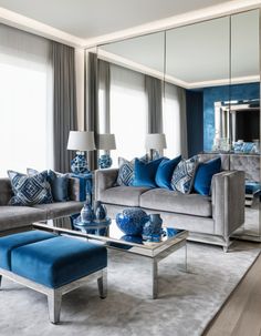 a living room filled with blue and gray furniture next to a large mirror on the wall