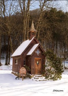 a small wooden church in the middle of a snow covered field with trees around it