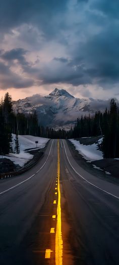 an empty road with snow covered mountains in the background