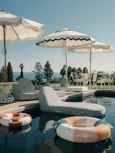 an outdoor pool with lounge chairs, umbrellas and inflatable floats on it