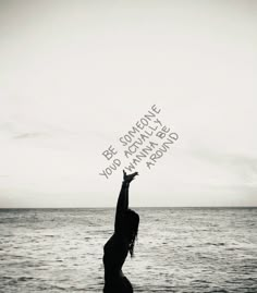 a woman standing on top of a beach next to the ocean holding her hand up in the air