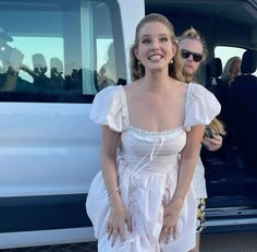 a woman in a white dress standing next to a van