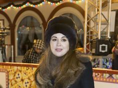 a woman with long hair wearing a fur hat and black coat standing in front of a mirror