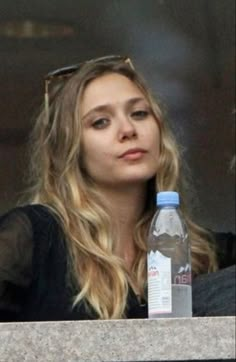 a woman sitting in front of a window with a water bottle next to her face