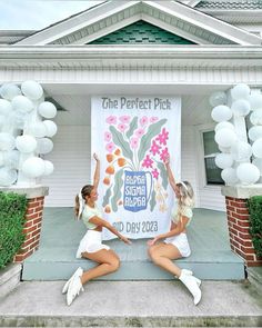 two beautiful women holding up a banner in front of a house with balloons on it