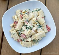 a white bowl filled with pasta and spinach on top of a wooden table next to a fork