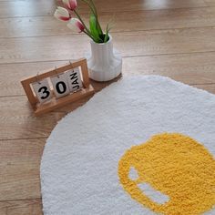 a yellow smiley face rug next to a white vase with tulips in it