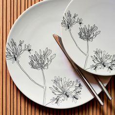 two plates with flowers painted on them sitting on a wooden table next to silverware