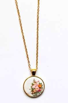 a necklace with flowers on it is hanging from a gold plated chain, against a white background