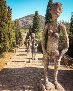 several statues in the shape of people walking down a stone path with trees on either side