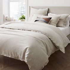 a bed with white linens and pillows in a bedroom next to a large window