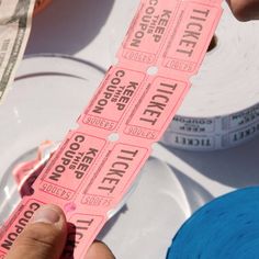 someone is holding two pink tickets in front of the camera and some money on the table