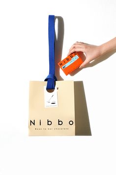 a hand holding an orange and blue bag with a name tag attached to the handle