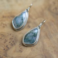 Natural, Moss Agate Drop Earrings. All metal is .925 Sterling Silver. Choose your pair below - your choice will be highlighted in the photo as you choose. These gorgeous, simple, Moss Agate drop earrings feature stunning and natural, Moss Agate irregularly shaped cabochons set in a simple .925 Sterling Silver bezel setting. Just Right! These deep earthy green Moss agate drop earrings switch from data to night while still having the richness and benefits of natural stones. We have pierced the bac Agate Gemstone Drop Earrings, Agate Drop Earrings, Agate Gemstone Dangle Earrings, Agate Gemstone Earrings Gift, Agate Gemstone Earrings For Gifts, Agate Drop Earrings With Matching Set, Trendy Agate Drop Earrings, Sterling Silver Pendant Earrings With Natural Stones, Chalcedony Natural Stone Drop Earrings