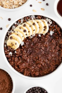 chocolate oatmeal with banana slices in a white bowl surrounded by other ingredients