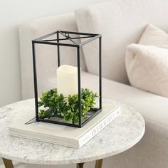 a table with a candle and some plants on it next to a white couch in a living room