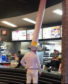 a man standing in front of a restaurant counter wearing a white suit and yellow hat