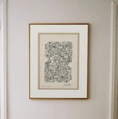 a framed print hangs on the wall above a toilet in a white bathroom with a wooden seat