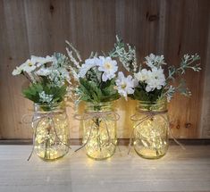 three mason jars filled with white flowers and greenery