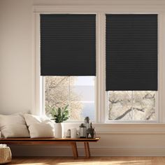 a living room with two windows that have black blinds on them, and a couch in front of the window