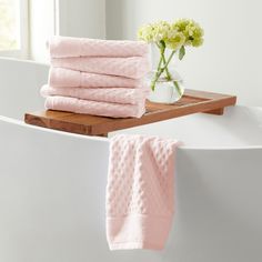 a stack of pink towels sitting on top of a bath tub next to a vase with flowers