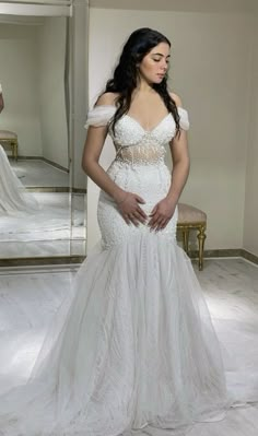 a woman in a wedding dress looking at herself in the mirror with her hands on her hips