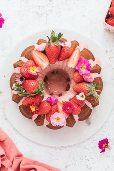 a bundt cake with strawberries and flowers on top, sitting on a white plate