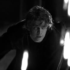 a man with curly hair and black shirt leaning over in front of some light bulbs