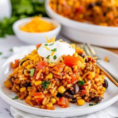 a white plate topped with mexican rice and beans next to a bowl of sour cream