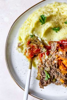 a white plate topped with mashed potatoes and meatloaf next to a fork