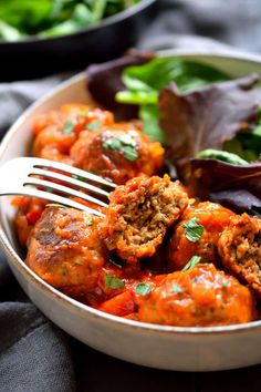 a white bowl filled with meatballs covered in sauce and garnished with parsley