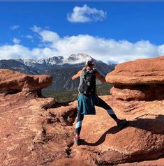 a person standing on top of a large rock formation with mountains in the back ground