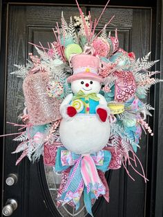 a snowman wreath is hanging on the front door with pink and green decorations around it