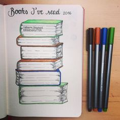 an open book sitting on top of a wooden table next to markers and pencils