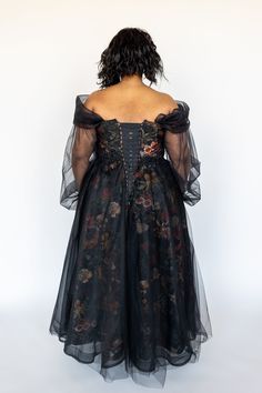 the back of a woman wearing a black dress with flowers on it and sheer sleeves