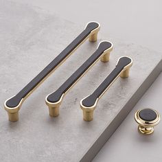 three handles and two knobs are shown on a gray surface with a gold ring