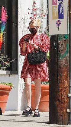 a woman in a red and white dress is looking at her cell phone while walking down the street